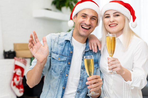 Caucasian couple at home together making a video call at christmas, wearing santa hats, smiling and waving. quality time together in covid