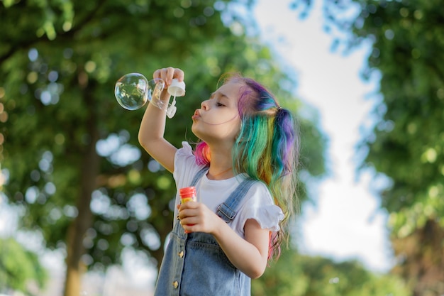 Caucasian cute little girl is blowing a soap bubbles in park. Image with selective focus