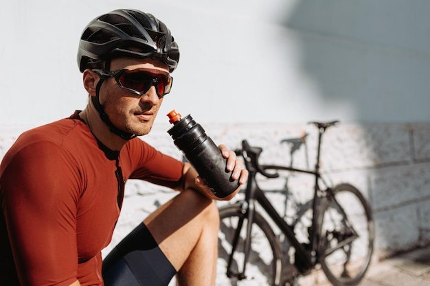 Caucasian cyclist in helmet and glasses drinking water from sport bottle while taking break during outdoors workout Refreshing after sport activity