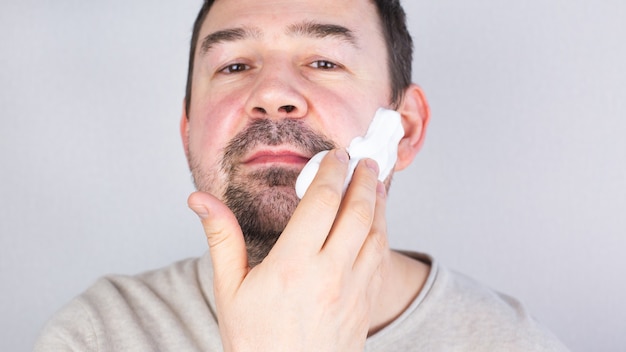 Caucasian darkhaired man applying shaving foam for his beard looking at camera smiling