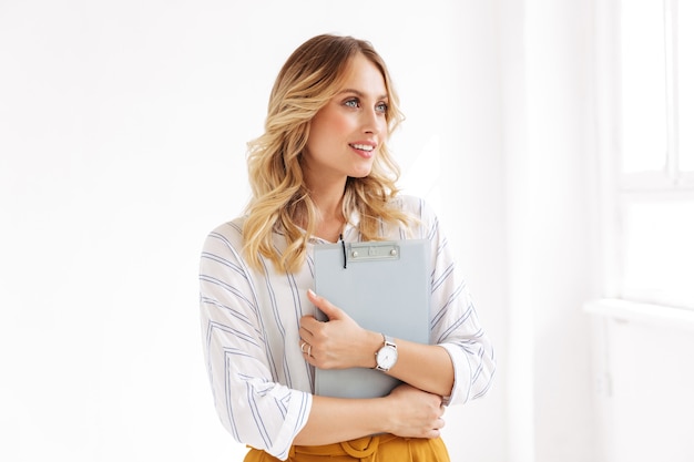 caucasian elegant woman smiling and holding clipboard in white office