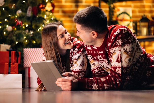 Caucasian family couple choosing christmas present online on tablet while lying at cozy home husband