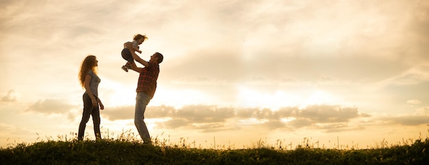 Caucasian family mom dad and little son at sunset Silhouettes of parents and toddler boy on the background of the sky Freedom and an active lifestyle