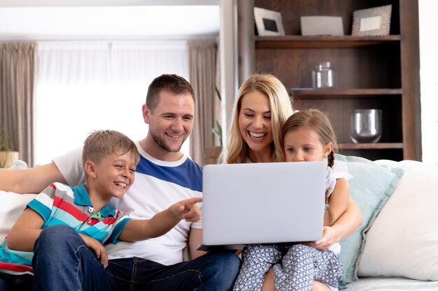 Caucasian family with two children spending time together at home, sitting on a couch and using a laptop computer. Social distancing and self isolation in quarantine lockdown.