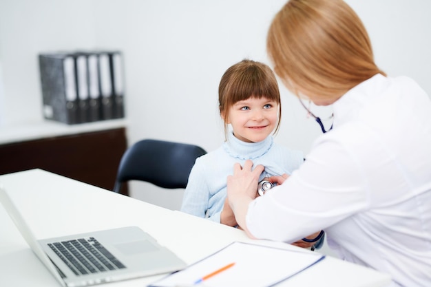 Caucasian female doctor examining patient little girl by stethoscope in office