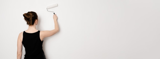 Caucasian female holding a painting roller. Woman painting a wall with roller banner