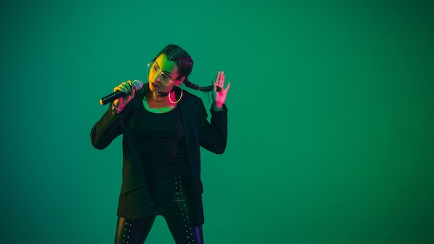 Caucasian female singer portrait isolated on green studio background in neon light