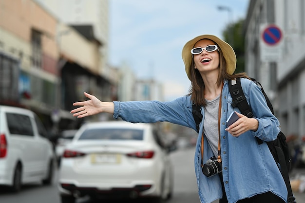 Caucasian female traveler raising hand calling taxi in busy city street Tourism and transportation concept