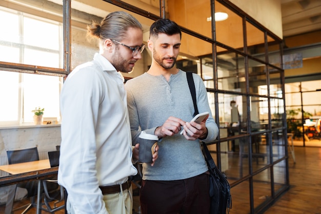 caucasian focused colleagues talking and using cellphone while standing in modern office