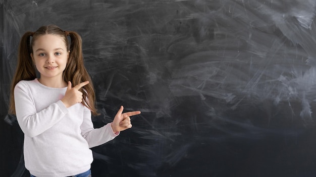 A Caucasian girl a schoolgirl is standing against the background of an empty chalk board the index finger points to an empty space for text