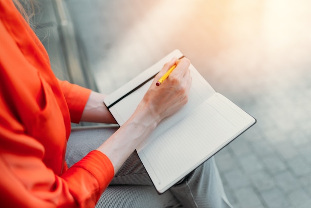 Caucasian girl sitting in the city and making notes in a notebook.