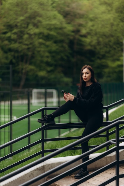 Caucasian girl in sport outfit is smiling and using her smart phone in a green park