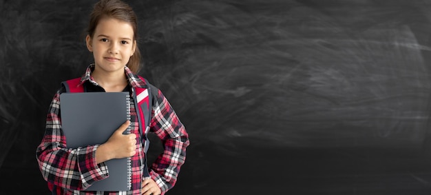 Caucasian girl student in the classroom near the chalk board He holds a notebook in his hands and looks at the camera Online education and elearning concept Back to school banner