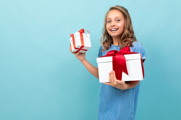 Photo caucasian girl with wavy brown hair in blue dress, big hat holds a boxes with gifts and rejoices