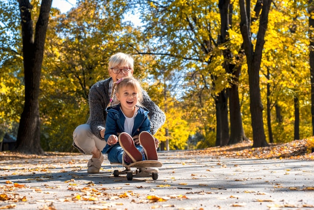 Caucasian granddaughter enjoying the day with grandmother while riding a skateboard in the park