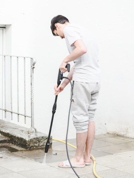 A caucasian guy in gray sports and a Tshirt from the back washes the stone tiles of the terrace