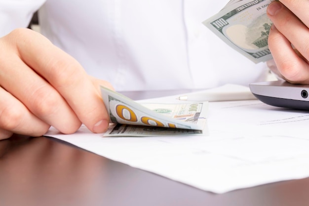 Caucasian hands counting dollar banknotes on white wooden surface