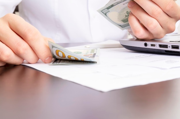 Caucasian hands counting dollar banknotes on white wooden surface