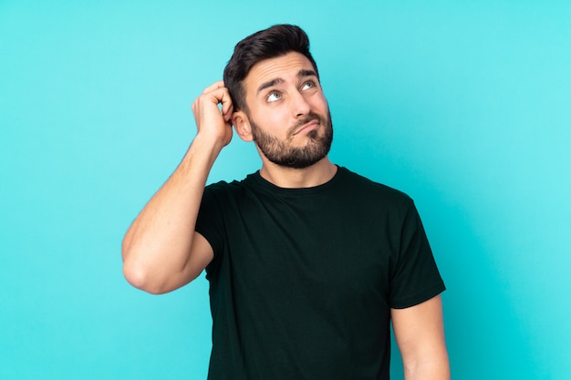 Caucasian handsome man on blue wall having doubts and with confused face expression