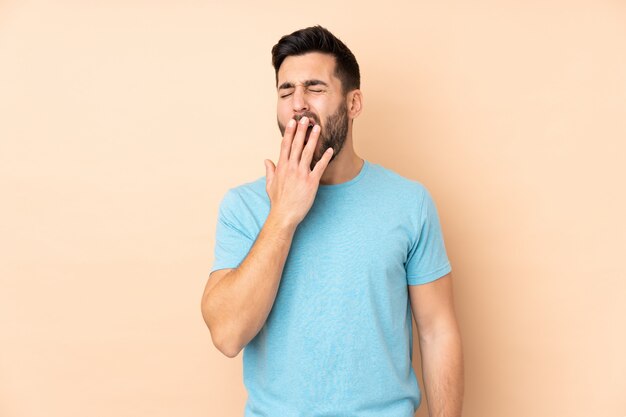 Photo caucasian handsome man isolated on beige wall yawning and covering wide open mouth with hand