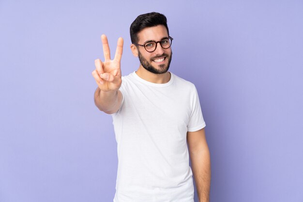 Caucasian handsome man over isolated wall smiling and showing victory sign