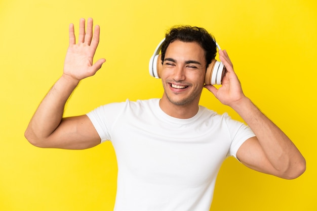 Caucasian handsome man over isolated yellow background listening music and dancing