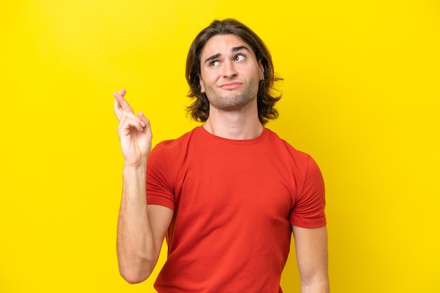 Caucasian handsome man isolated on yellow background with fingers crossing and wishing the best