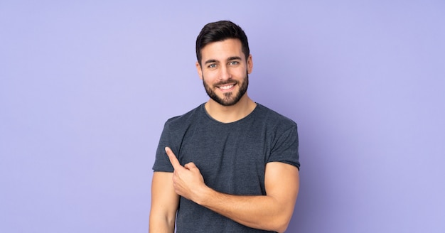 Caucasian handsome man pointing to the side over purple wall