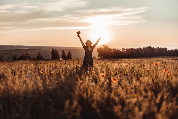 Caucasian Happy beautiful young girl with a poppy bouquet in her hands in a summer field at sunset. Tourism, traveling and healthy lifestyle concept.