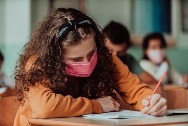 Caucasian kid school girl wearing face mask studying in the classroom