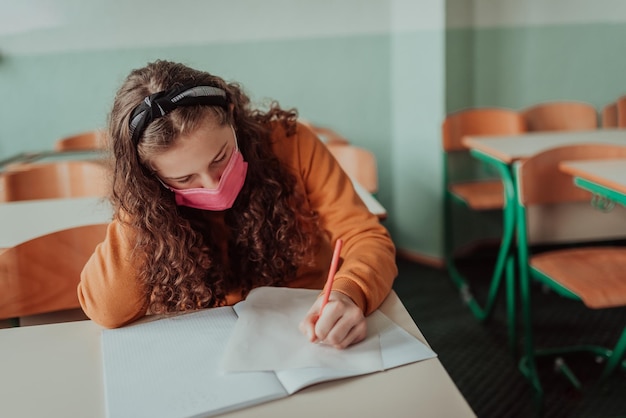 Caucasian kid school girl wearing face mask studying in the classroom