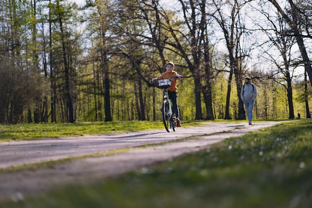 Caucasian little boy riding a bicycle with basket Father walking in distance