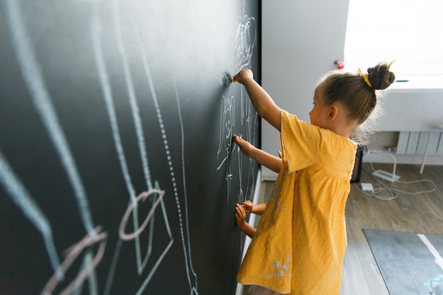 Caucasian little girl draws on the wall with chalkboard