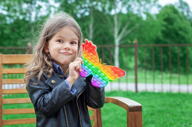 Caucasian little girl playing with pop it silicone trendy rainbow colow toy