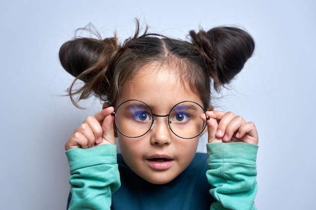 Caucasian little girl wearing glasses squinting while looking at camera isolated on white background Vision problems concept