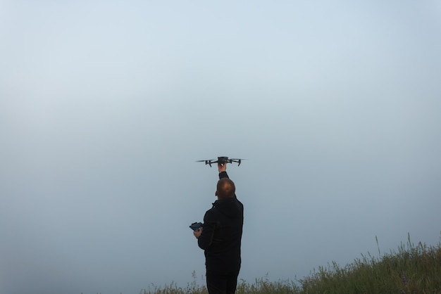 Caucasian male catching or launching portable contemporary drone at foggy summer morning