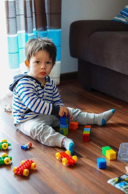 Caucasian male toddler playing with his colorful plastic toys on the woden floor