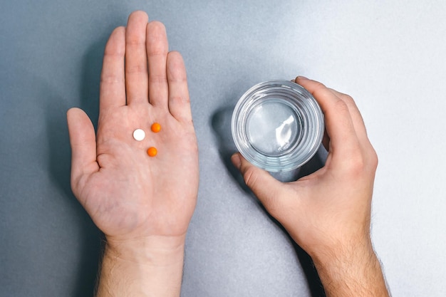 Caucasian male with two orange and one white pills in left palm and glass of water in right hand