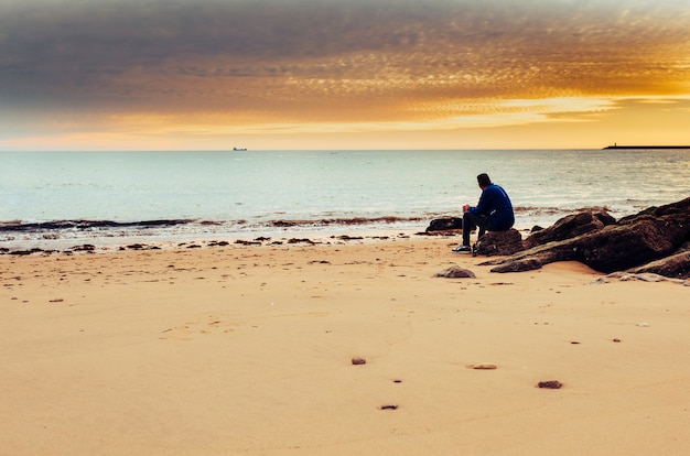 Photo caucasian man alone sitting on the shore of the sea