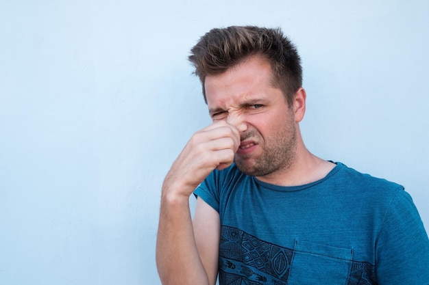 Caucasian man in blue shirt closing his nose because of bad smell