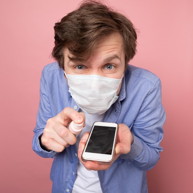 Caucasian man disinfecting his smartphone by spraying a sanitizer from a bottle