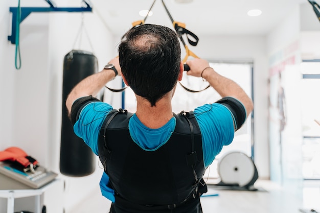 Caucasian man doing push-ups on a rope while wearing an electrostimulation suit