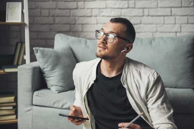 Caucasian man in eyewear using mobile phone while working sitting on the floor listening music with