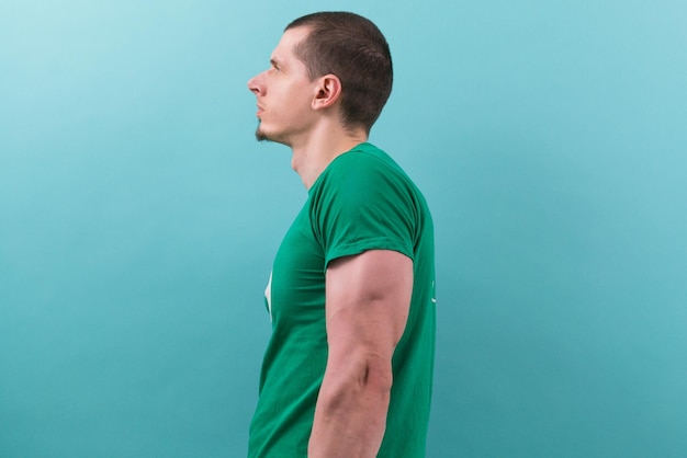 A caucasian man in a green t-shirt with big arm stands side on a blue Muscle Triceps