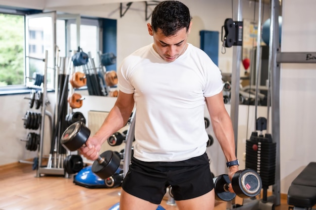 A caucasian man in the gym in a white tshirt lifting weights healthy and healthy life doing sports