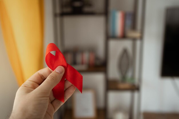 Caucasian man hand holding red aids ribbon.