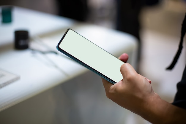 A caucasian man holds new smartphone with white screen copyspace close up soft focus background in