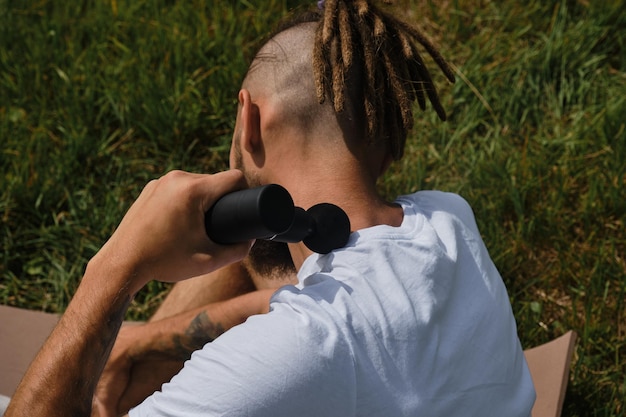 Caucasian man massages himself with percussion gun outside