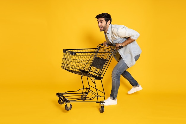 Caucasian man pushing an empty shopping cart or shopping trolley isolated on yellow background