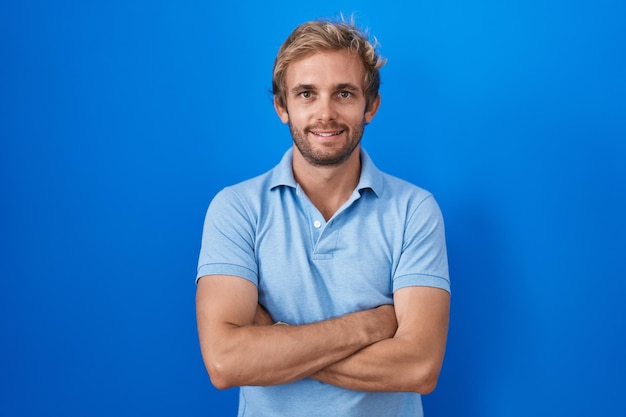 Caucasian man standing over blue background happy face smiling with crossed arms looking at the camera. positive person.